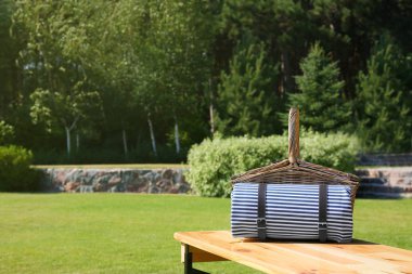 Yeşil parkta ahşap masa üzerinde battaniye ile piknik sepeti