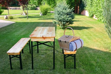 Yeşil bahçede masa yakınında ahşap bankta battaniye ile piknik sepeti