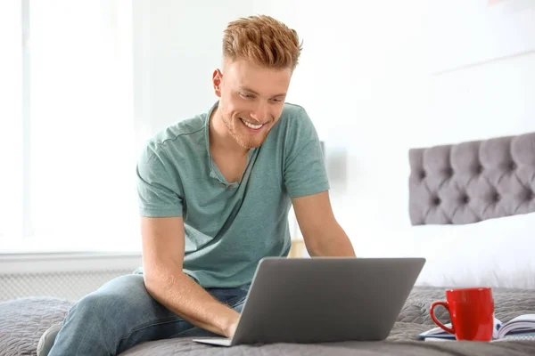 Junger Mann benutzt Laptop, während er zu Hause auf dem Bett sitzt — Stockfoto