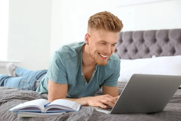 Junger Mann benutzt Laptop, während er zu Hause im Bett liegt — Stockfoto