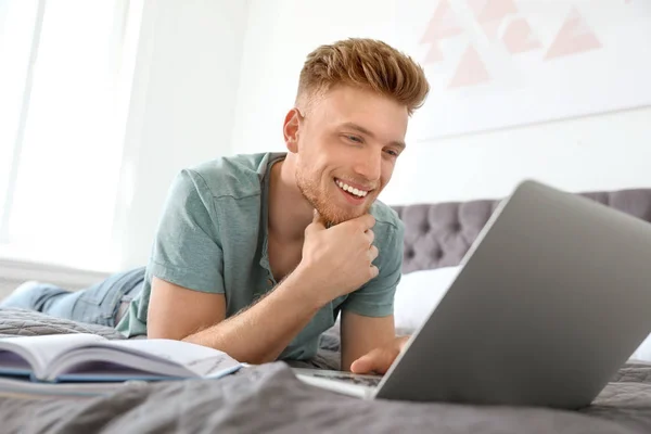 Young man using laptop while lying on bed at home — Stock Photo, Image