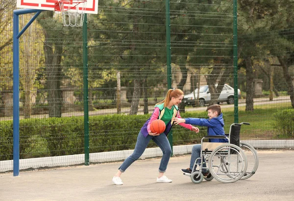 Niño preadolescente en silla de ruedas y mujer joven jugando baloncesto en el campo de deportes — Foto de Stock