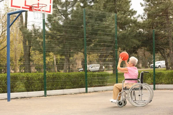 Starsza kobieta na wózku inwalidzkim gra w koszykówkę na ziemi sportowej — Zdjęcie stockowe
