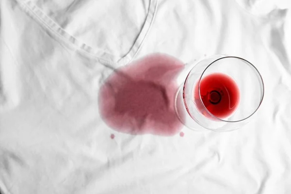 Transparent glass and spilled exquisite red wine on white t-shirt, top view. Space for text — Stock Photo, Image