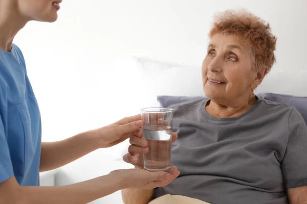 Enfermera dando vaso de agua a anciana en el interior. Asistencia médica — Foto de Stock