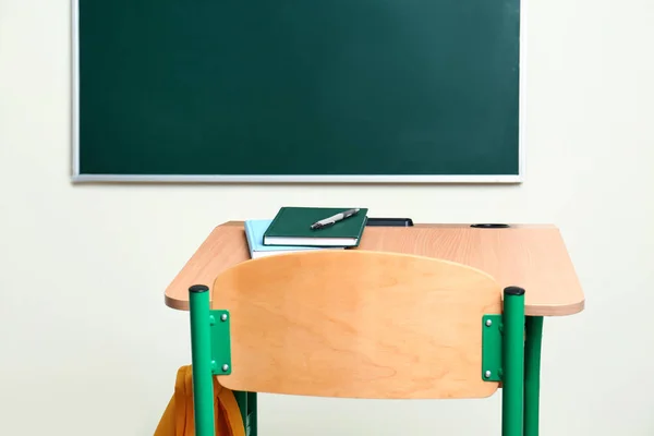 Bureau scolaire avec papeterie et sac près du tableau dans la salle de classe — Photo