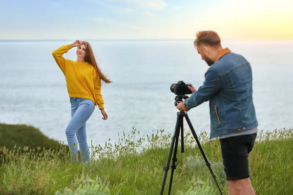 Мужской фотограф фотографирует молодую женщину с профессиональной камерой на открытом воздухе — стоковое фото