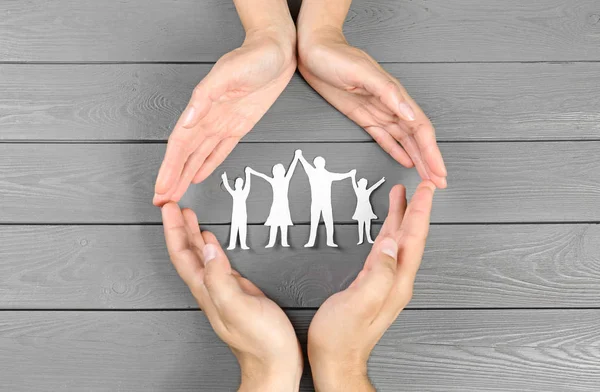 Jonge man en vrouw beschermen papier familie figuur met hun handen op grijze houten achtergrond, Top View — Stockfoto