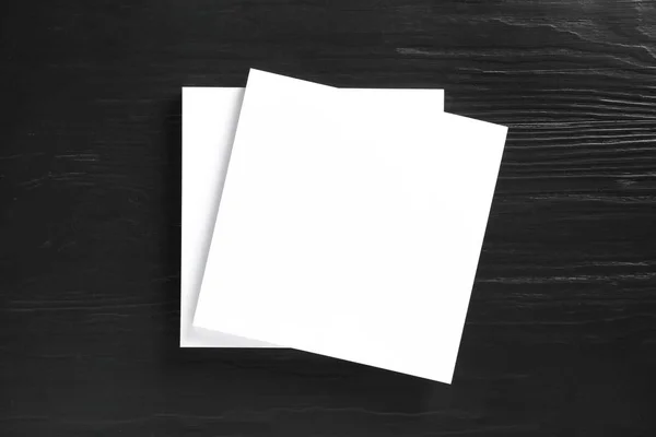 Pilha de folhas de papel em branco para brochura sobre fundo de madeira preta, vista superior. Faz asneira. — Fotografia de Stock