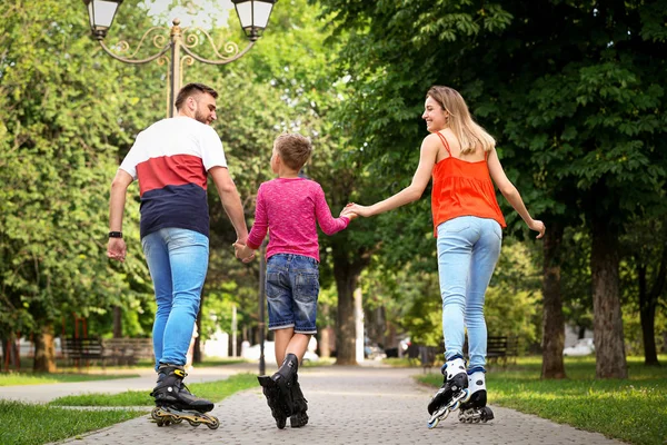 Young family roller skating in park, back view Royalty Free Stock Images