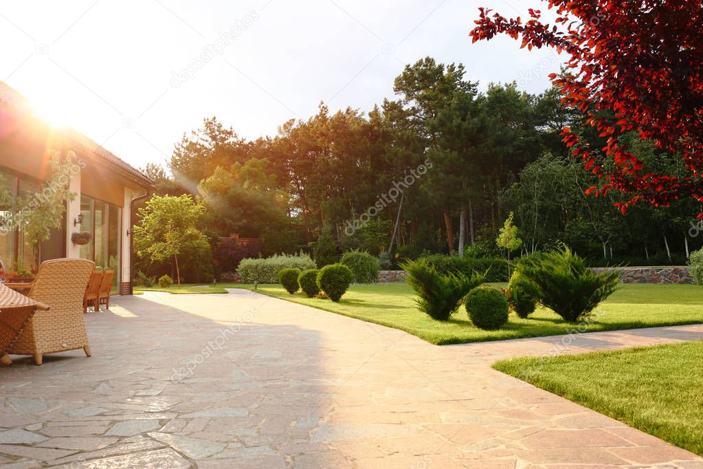 Picturesque landscape with beautiful green garden near house on sunny day