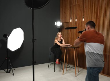 Profesyonel fotoğrafçı modern stüdyoda genç kadının fotoğrafını çekiyor