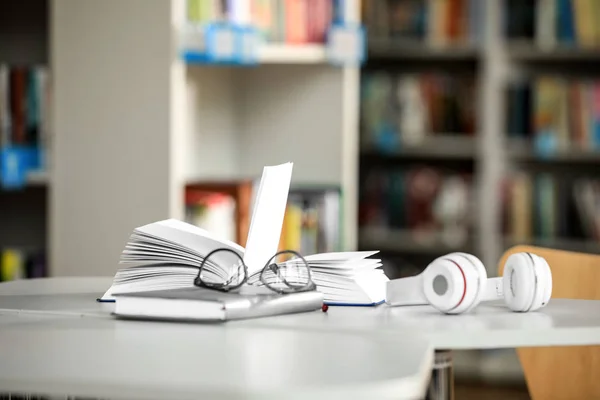 Livros, óculos e fones de ouvido na mesa da biblioteca — Fotografia de Stock