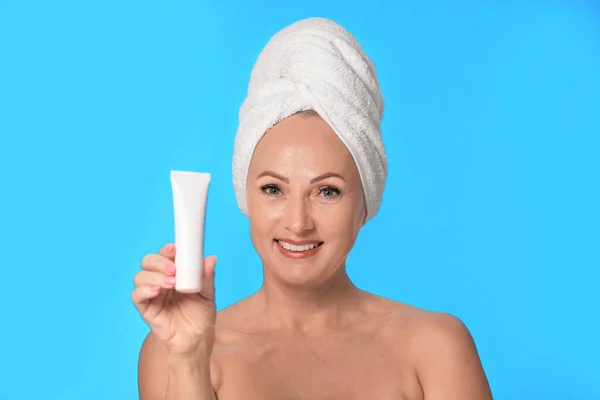 Portret van mooie rijpe vrouw met perfecte huid houden buis van crème op licht blauwe achtergrond — Stockfoto