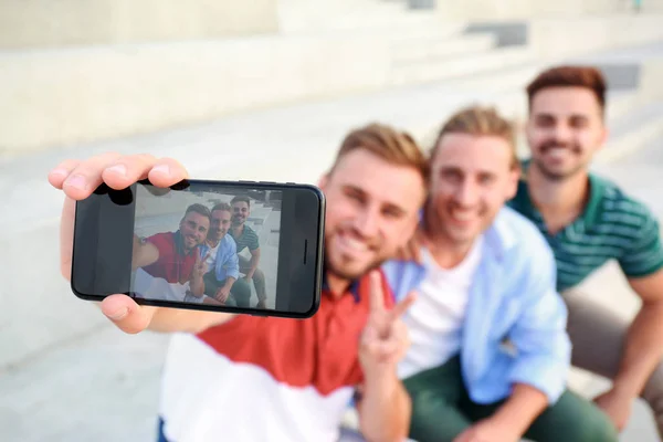 Hombres jóvenes felices tomando selfie al aire libre, se centran en el teléfono inteligente — Foto de Stock