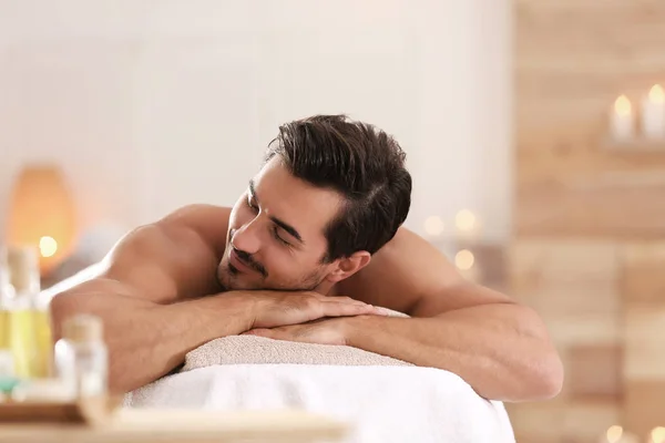 Bonito jovem relaxante na mesa de massagem no salão de spa, espaço para texto — Fotografia de Stock