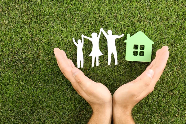 Man holding hands near figures of house and family on green grass, top view