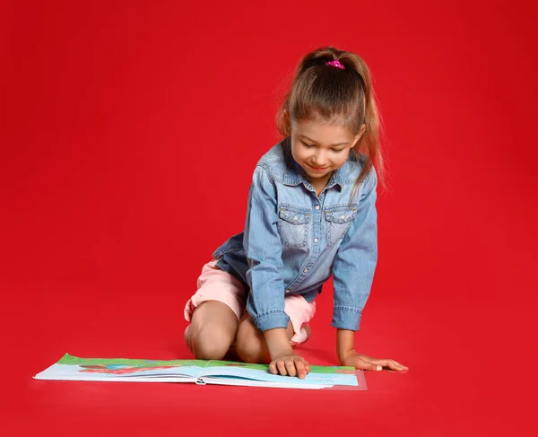 Linda niña leyendo libro sobre fondo rojo — Foto de Stock