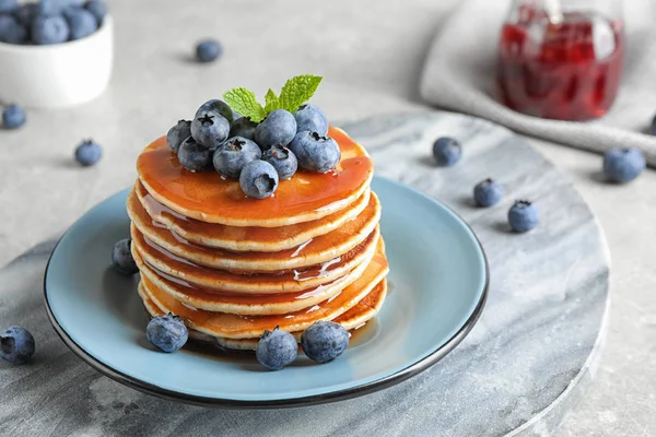 Assiette de délicieuses crêpes aux bleuets frais et sirop sur table grise — Photo