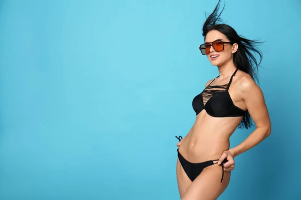 Piękna młoda kobieta w stylowym bikini z okulary przeciwsłoneczne na jasnym niebieskim tle. Miejsce na tekst — Zdjęcie stockowe