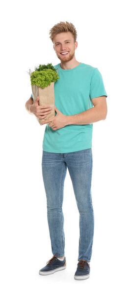 Young man with bag of fresh vegetables on white background