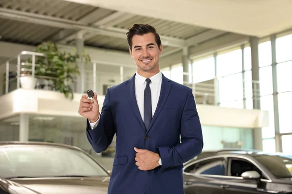 Joven vendedor con llave de coche en concesionario moderno — Foto de Stock