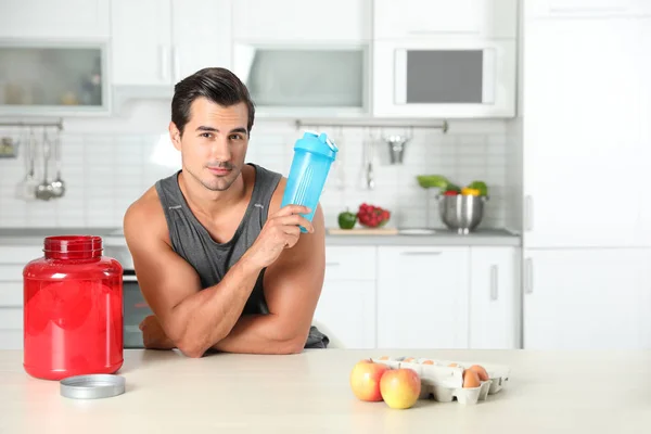 Homem atlético jovem com ingredientes para batido de proteína na cozinha, espaço para texto — Fotografia de Stock