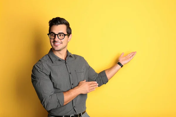 Young male teacher with glasses on yellow background. Space for text