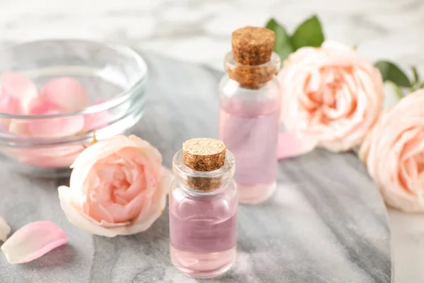 Garrafas com óleo essencial de rosa e flores em placa de pedra — Fotografia de Stock