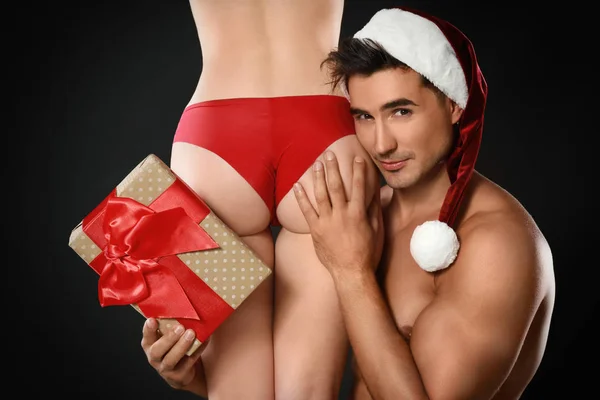 Attractive young Santa Claus with sexy woman and gift on dark background — Stock Photo, Image