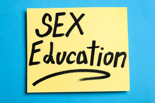 Nota con la frase "SEXO EDUCACIÓN" sobre fondo azul, vista superior — Foto de Stock