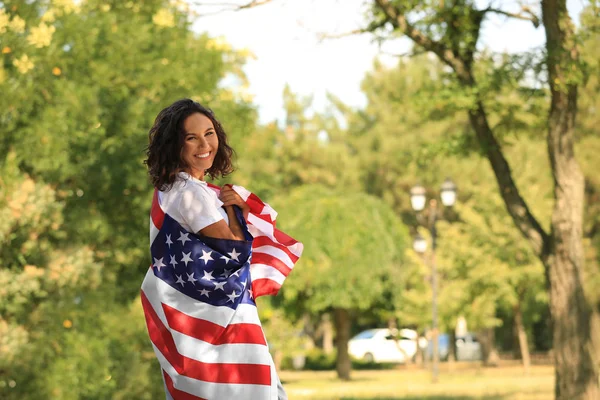 Szczęśliwa młoda kobieta z amerykańską flagą w parku w słoneczny dzień — Zdjęcie stockowe