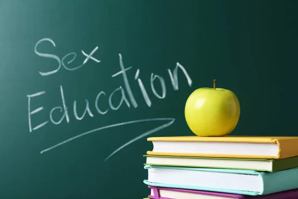 Livros e maçã perto de quadro-negro com frase "Educação sexual " — Fotografia de Stock