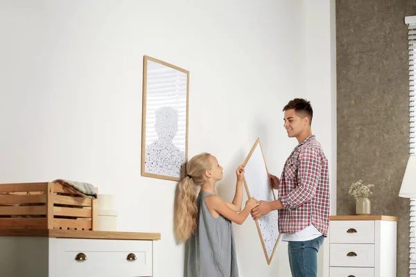 Klein meisje helpt haar vader te hangen schilderen op de muur thuis — Stockfoto