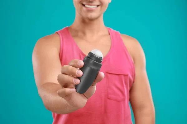 Young man holding deodorant on blue background, closeup. Mockup for design — Stock Photo, Image