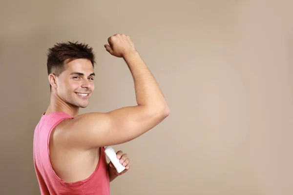 Young man applying  deodorant to armpit on beige background. Space for text