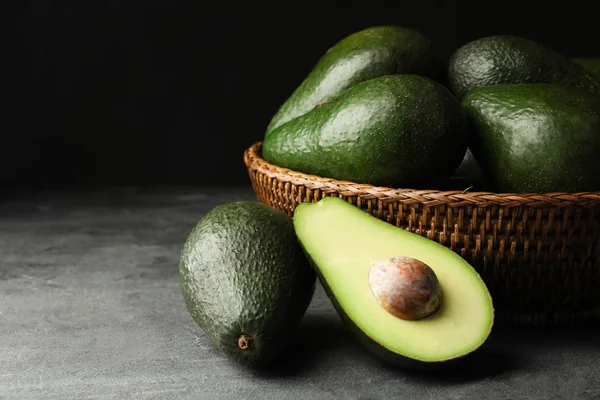 Deliziosi avocado maturi su tavolo grigio su sfondo scuro — Foto Stock