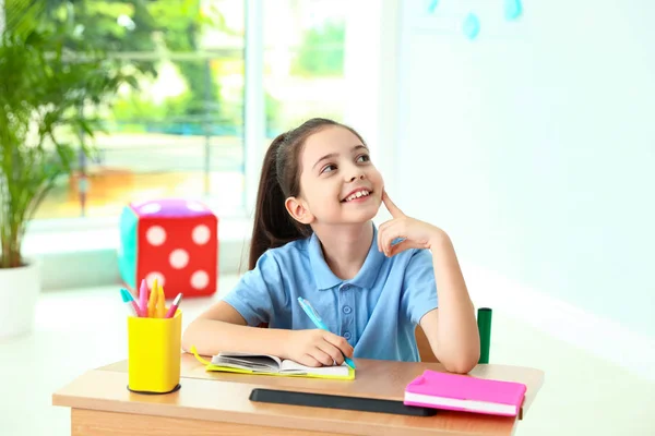 Nachdenkliches kleines Mädchen, das am Schreibtisch im Klassenzimmer Aufgaben erledigt. Schulschreibwaren — Stockfoto