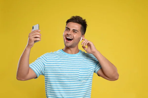 Joven feliz con smartphone escuchando música a través de auriculares inalámbricos sobre fondo amarillo — Foto de Stock