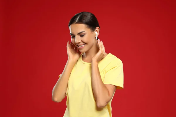 Happy young woman listening to music through wireless earphones on red background — Stock Photo, Image