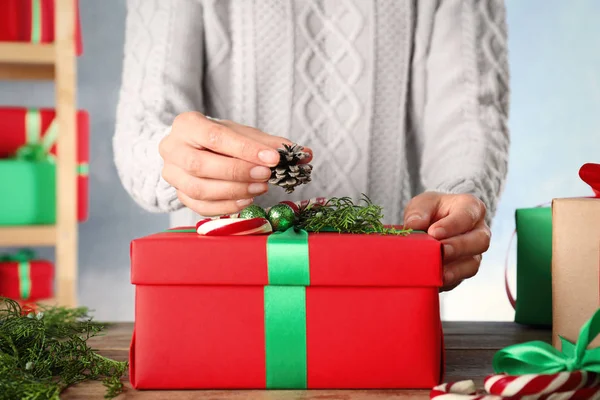 Женщина упаковывает рождественский подарок за деревянным столом в помещении, крупным планом — стоковое фото
