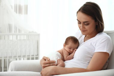 Küçük bebeği evde koltukta oturan genç anne. Metin için alan