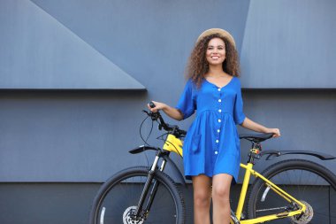 Şehir caddesinde gri duvarın yanında bisikletli güzel genç Afro-Amerikalı kadın. Metin için alan