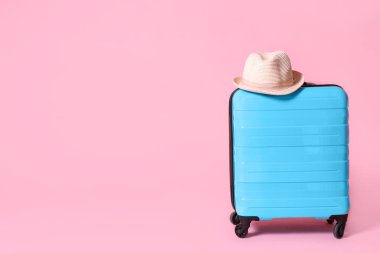 Modern mavi bavul ve açık pembe arka plan üzerinde şapka. Metin için alan