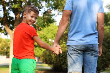 Küçük çocuk ve babası dışarıda el ele tutuşuyorlar. Aile hafta sonu