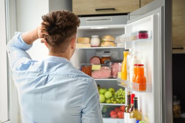 Adam mutfakta ürünlerle dolu buzdolabı içine bakıyor