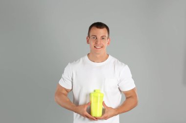 Açık gri arka planda protein sallamak ile Atletik genç adam