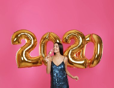 Pembe arka plan üzerinde altın 2020 balonlar yakın şampanya cam ile Mutlu genç kadın. Yeni Yıl kutlaması