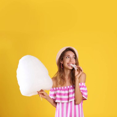 Mutlu genç kadın sarı arka plan üzerinde pamuk şeker yemek