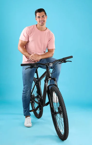 Przystojny młody człowiek z nowoczesnym rowerem na jasnym niebieskim tle — Zdjęcie stockowe